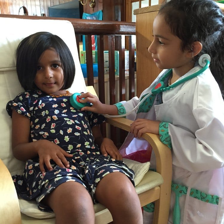 Child in doctor costume using toy stethoscope on another child