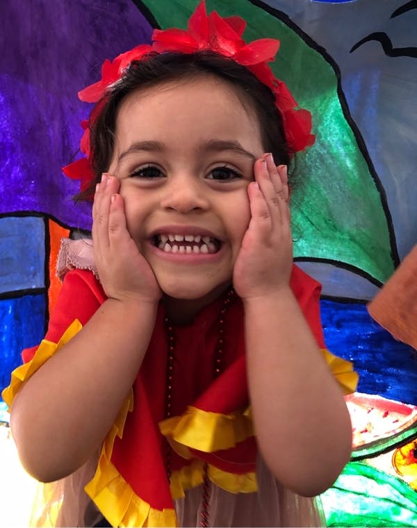Child in a red and yellow top with a red flower headband, hands on cheeks