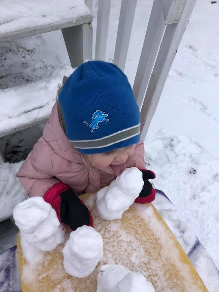 Child in a blue hat and pink coat playing with snow on a sled