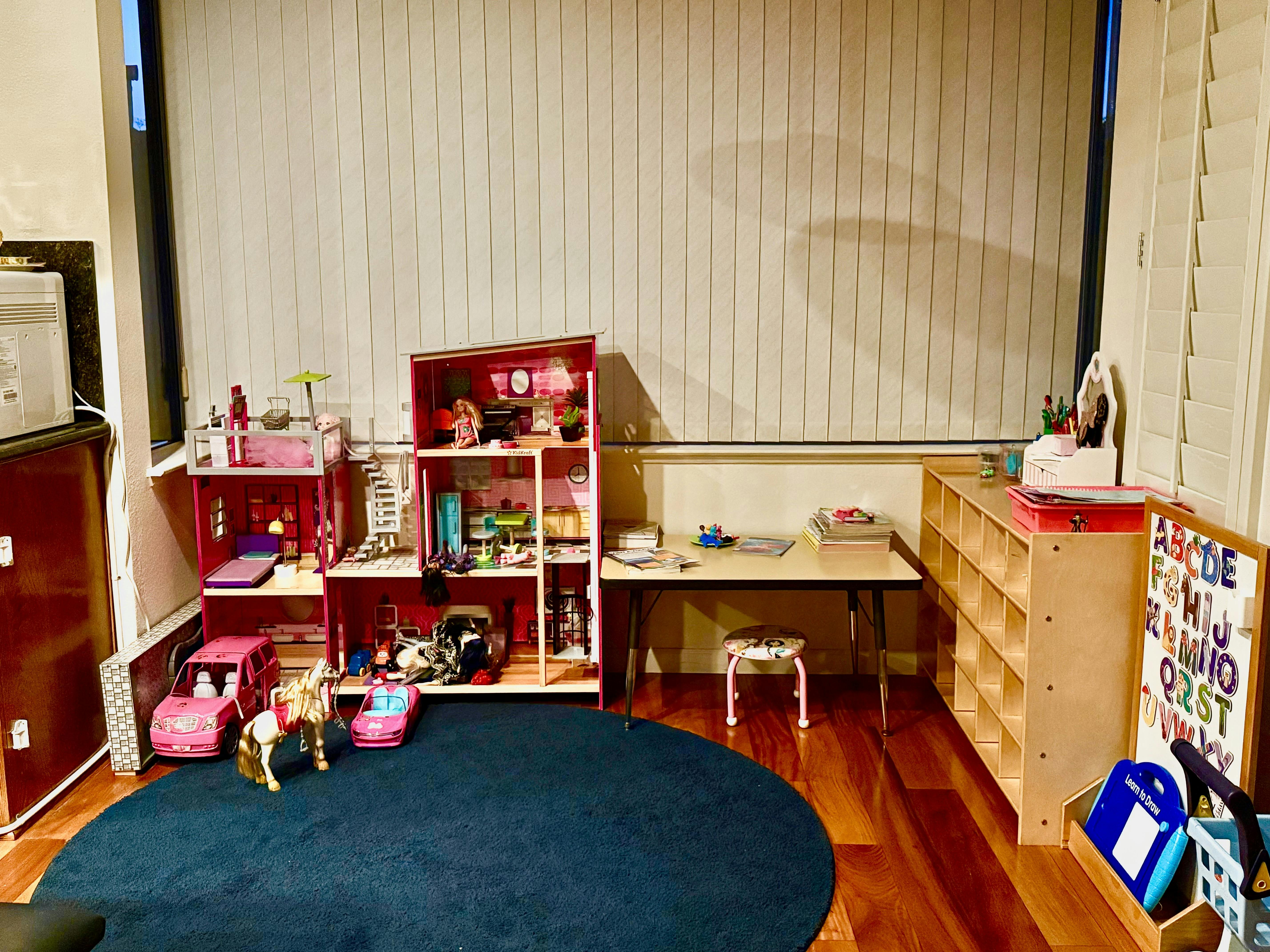 Dollhouse, toy cars, and table with books in a play area