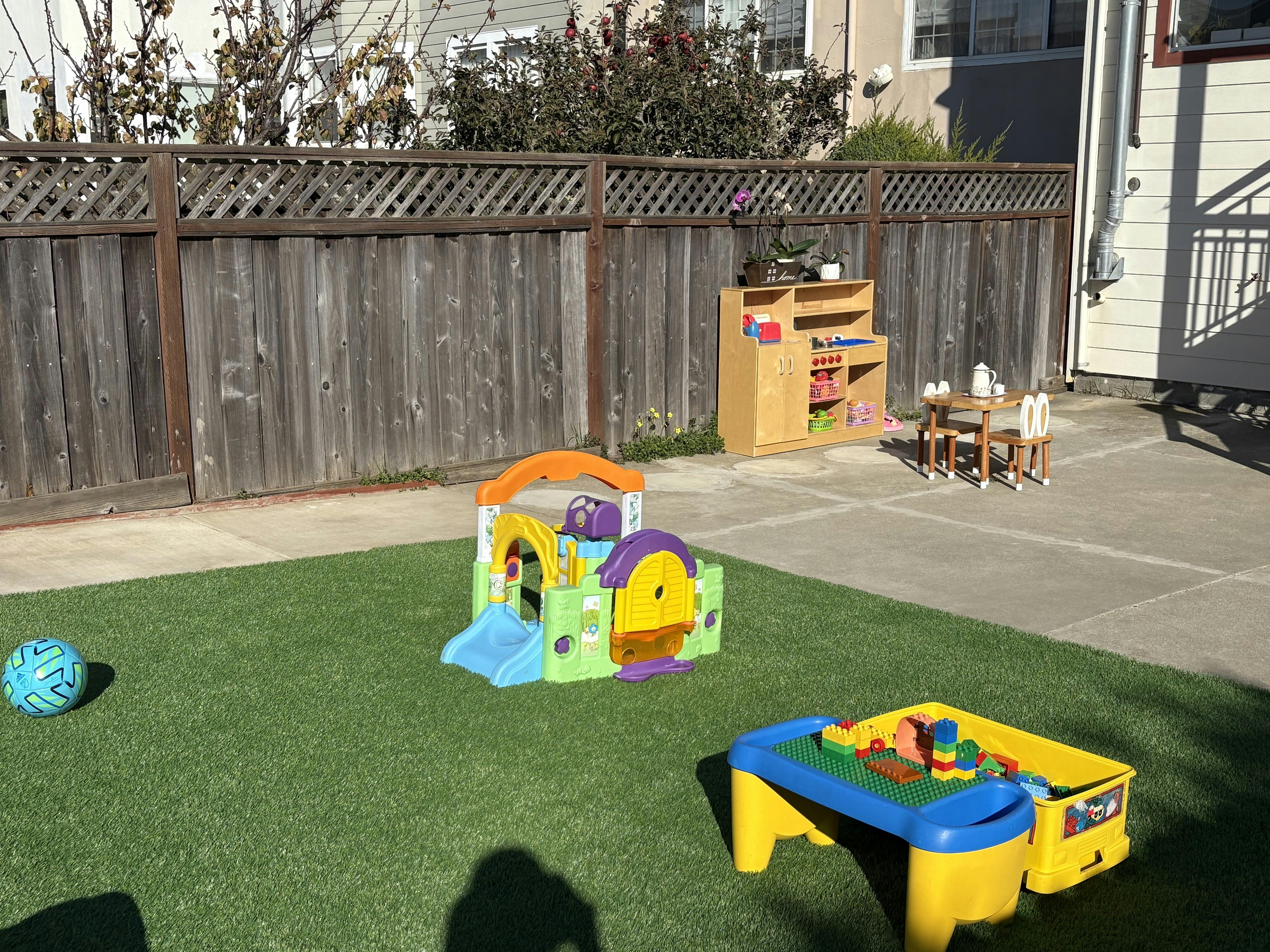 Playground with a colorful playhouse, blue ball, and activity table on artificial grass