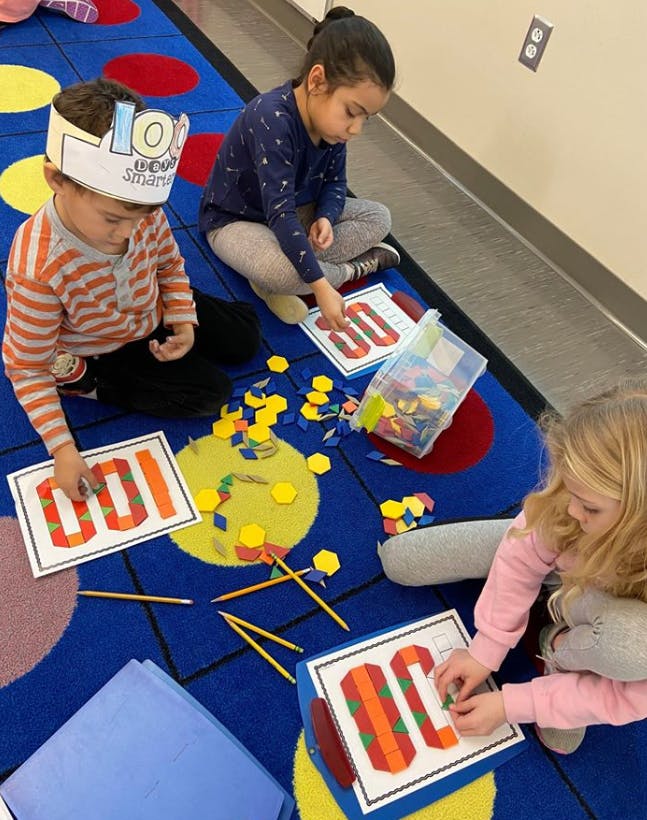 Three children on a rug doing an activity with number cards and small shapes