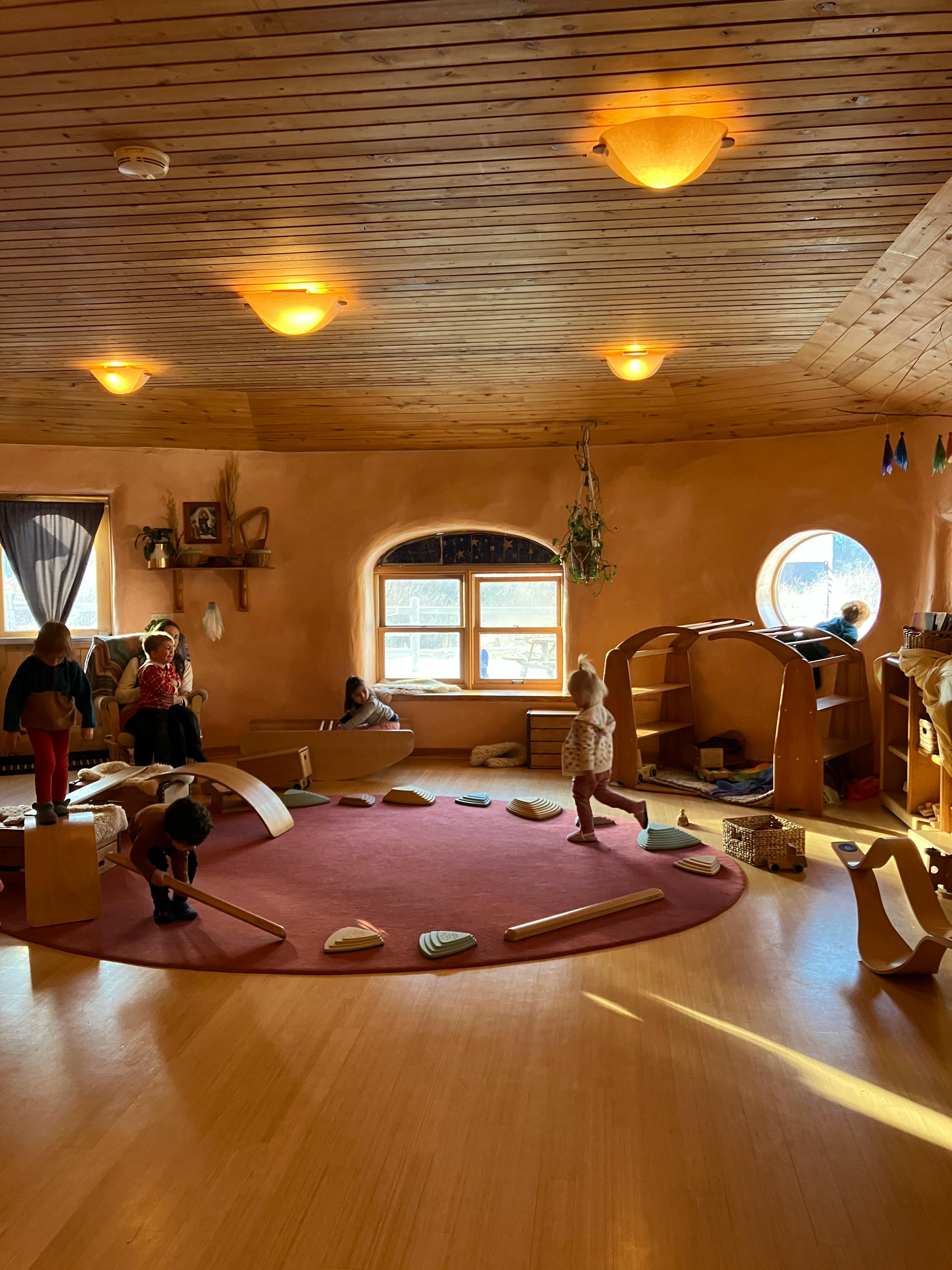 Children playing in a classroom with wooden furniture and a round rug