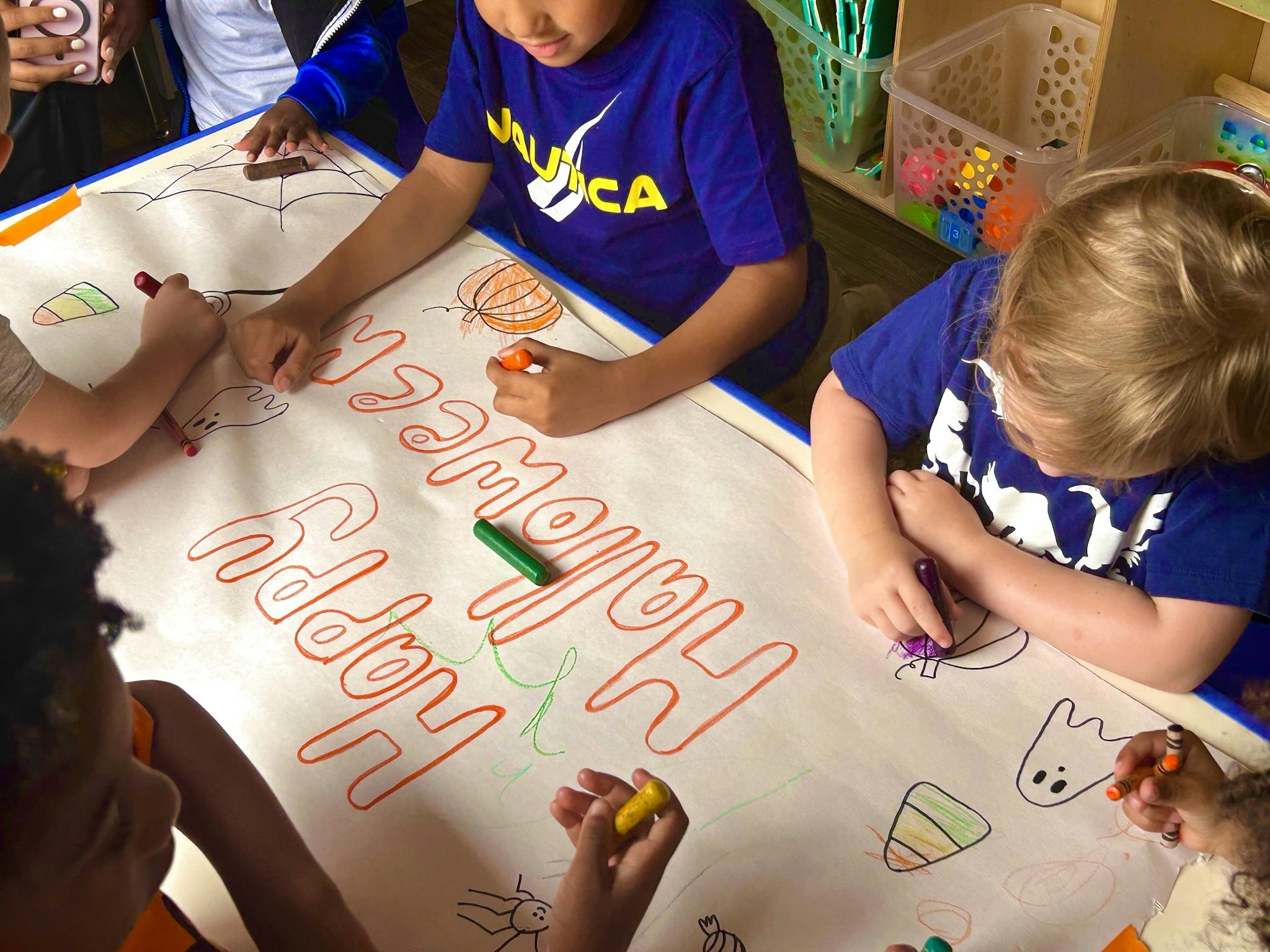 Children coloring a large banner that says "Happy Halloween"