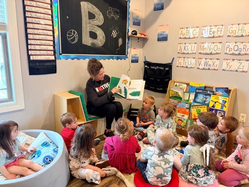 person reading a storybook to a group of children in a classroom