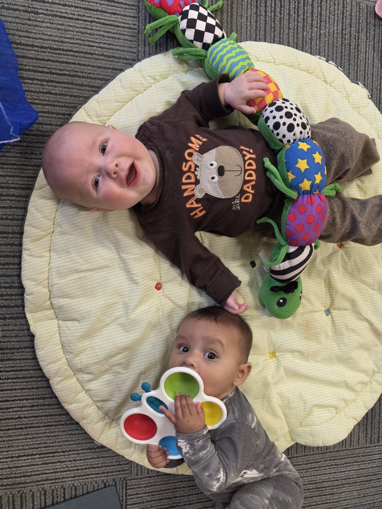 Two babies playing on a mat with toys