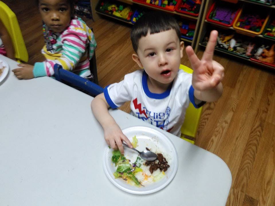 Child eating at a table, holding up two fingers