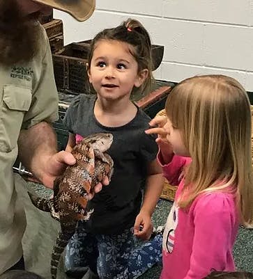 Person holding a lizard with two children looking at it