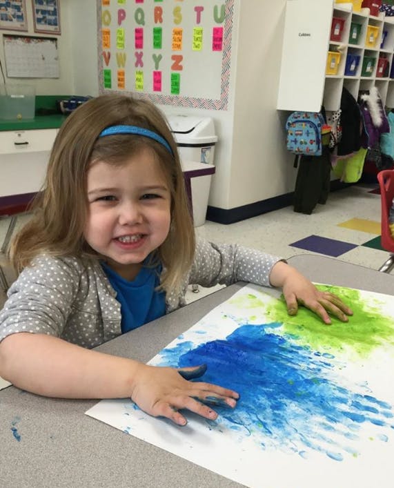 Child finger painting with blue and green paint on paper