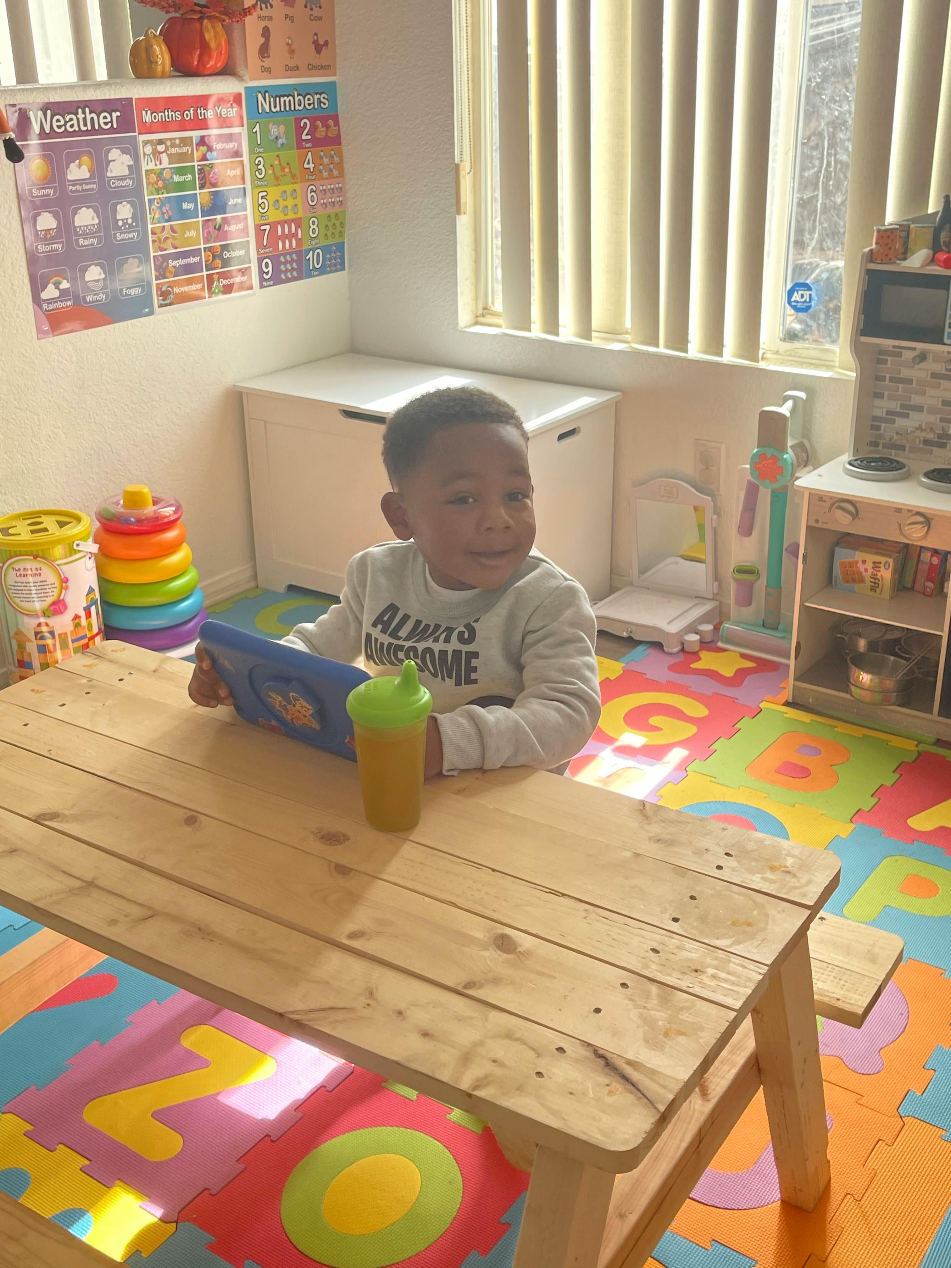 Child sitting at a table with a tablet and a cup
