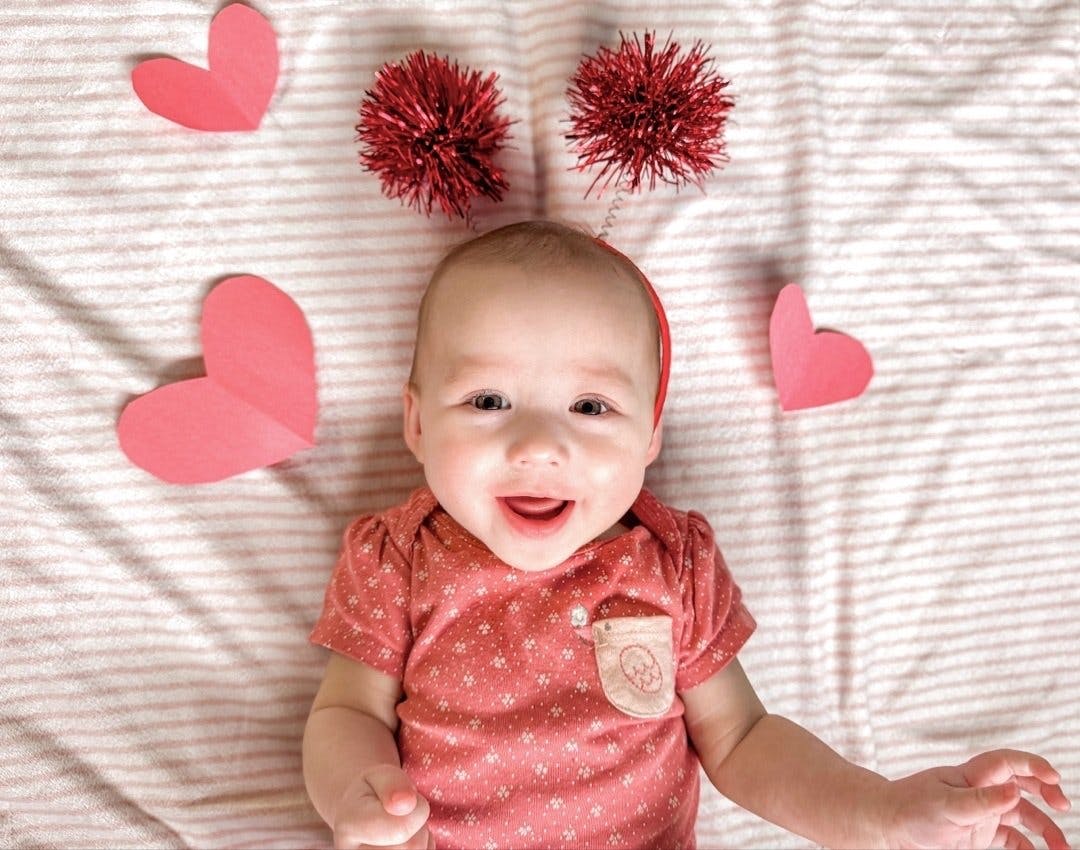 Child lying on back with red pom-poms above head and paper hearts around