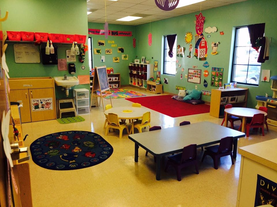 Classroom with small tables and chairs, a red rug, and decorations on the walls