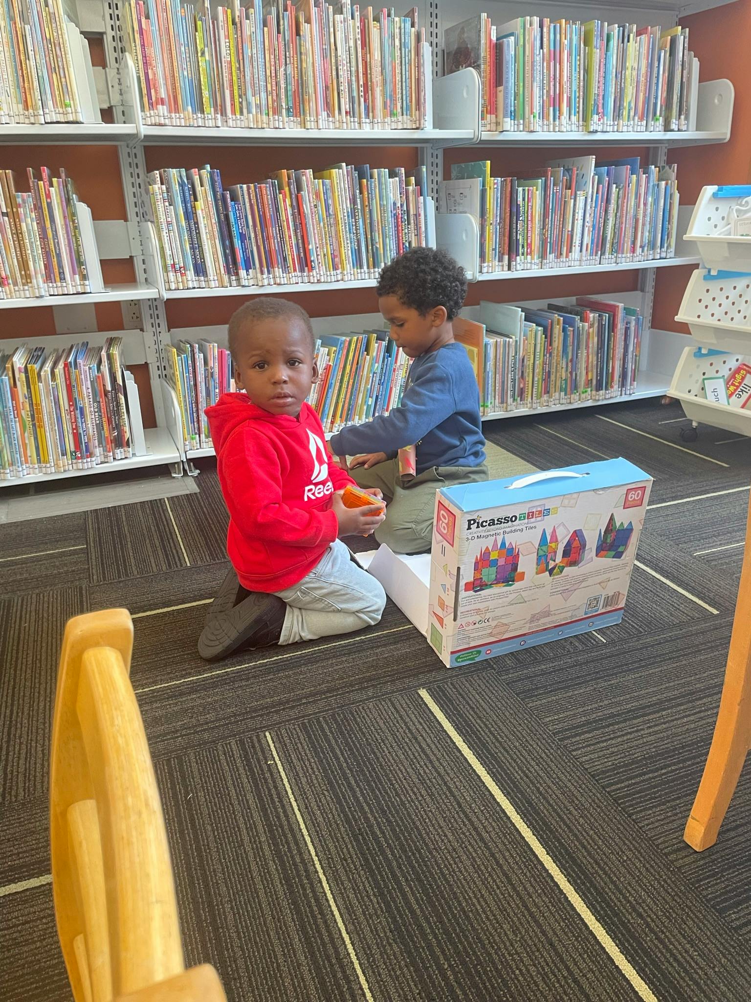 Two children playing with toys on the floor in a library