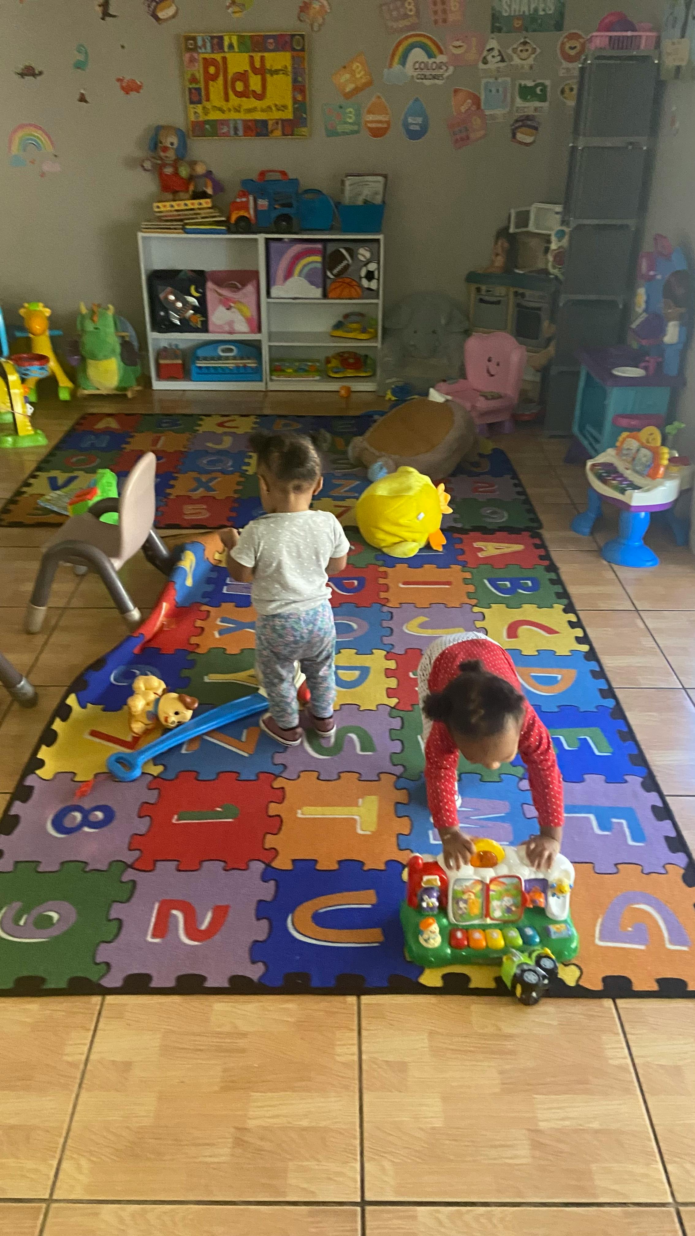 Two children playing on an alphabet mat in a playroom