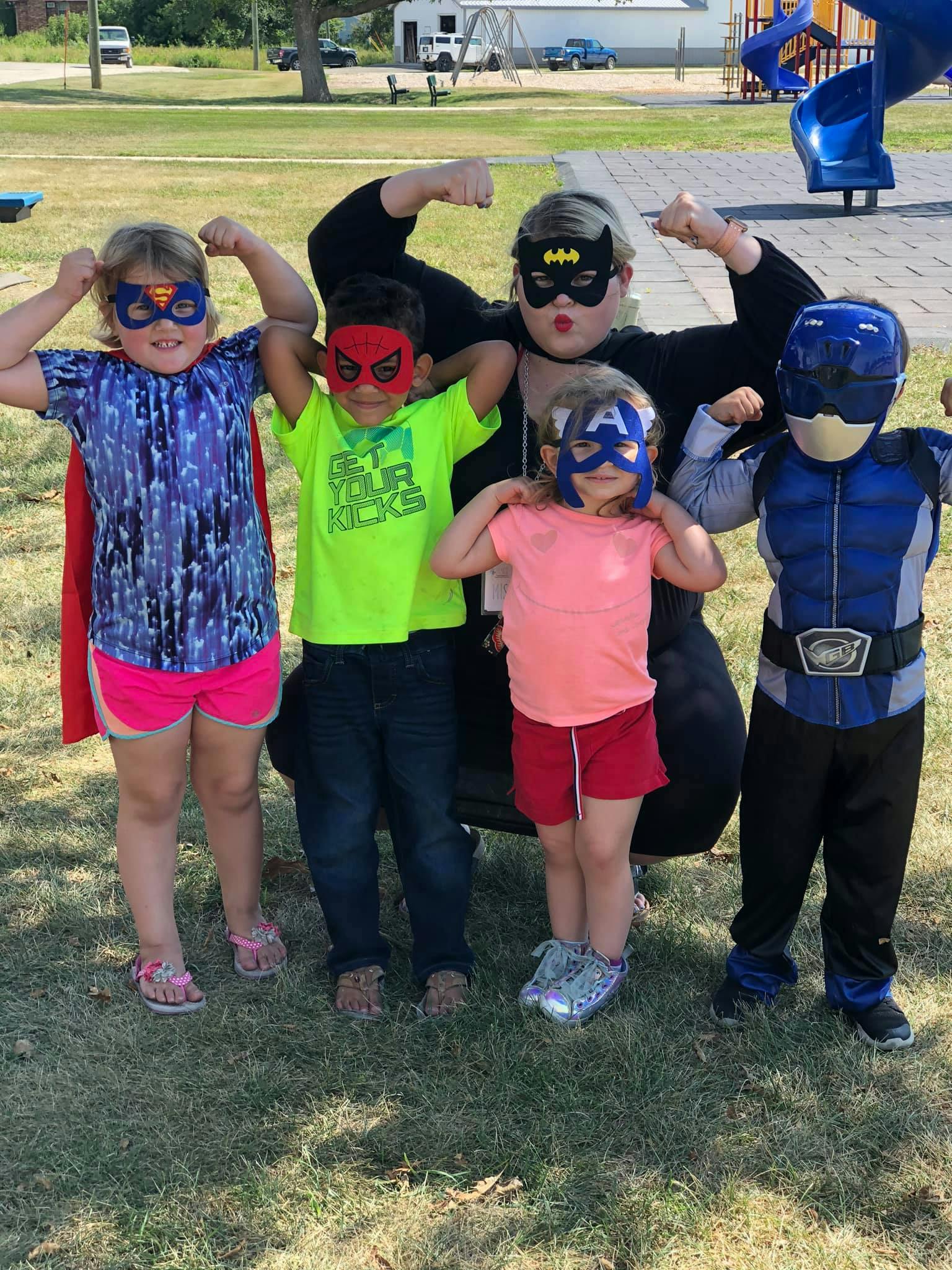 Four children and one adult in superhero masks and costumes flexing their arms