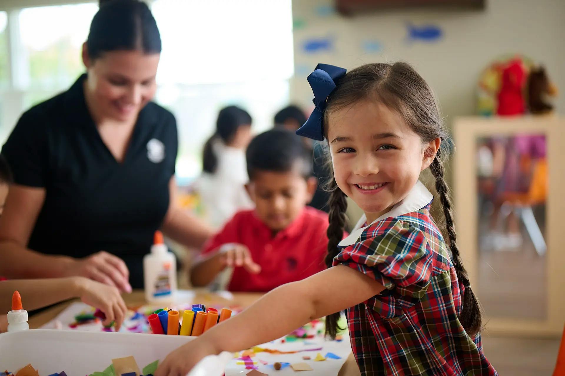 Child smiling at camera while doing crafts with other children and an adult