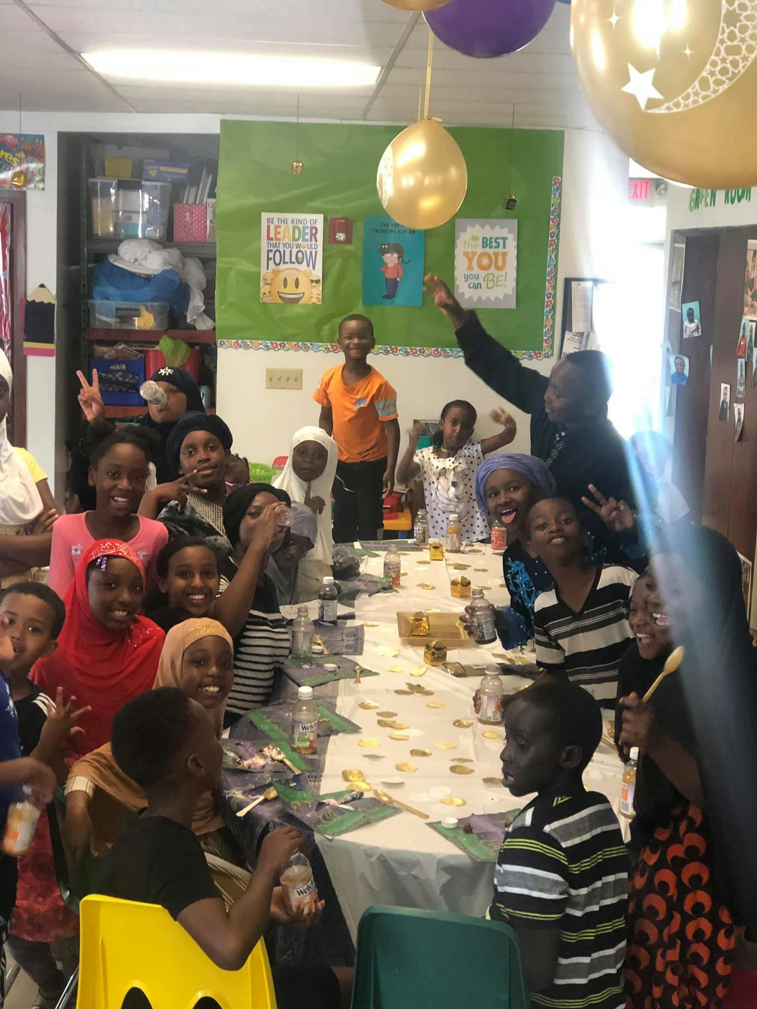 Group of children and adults gathered around a table with balloons