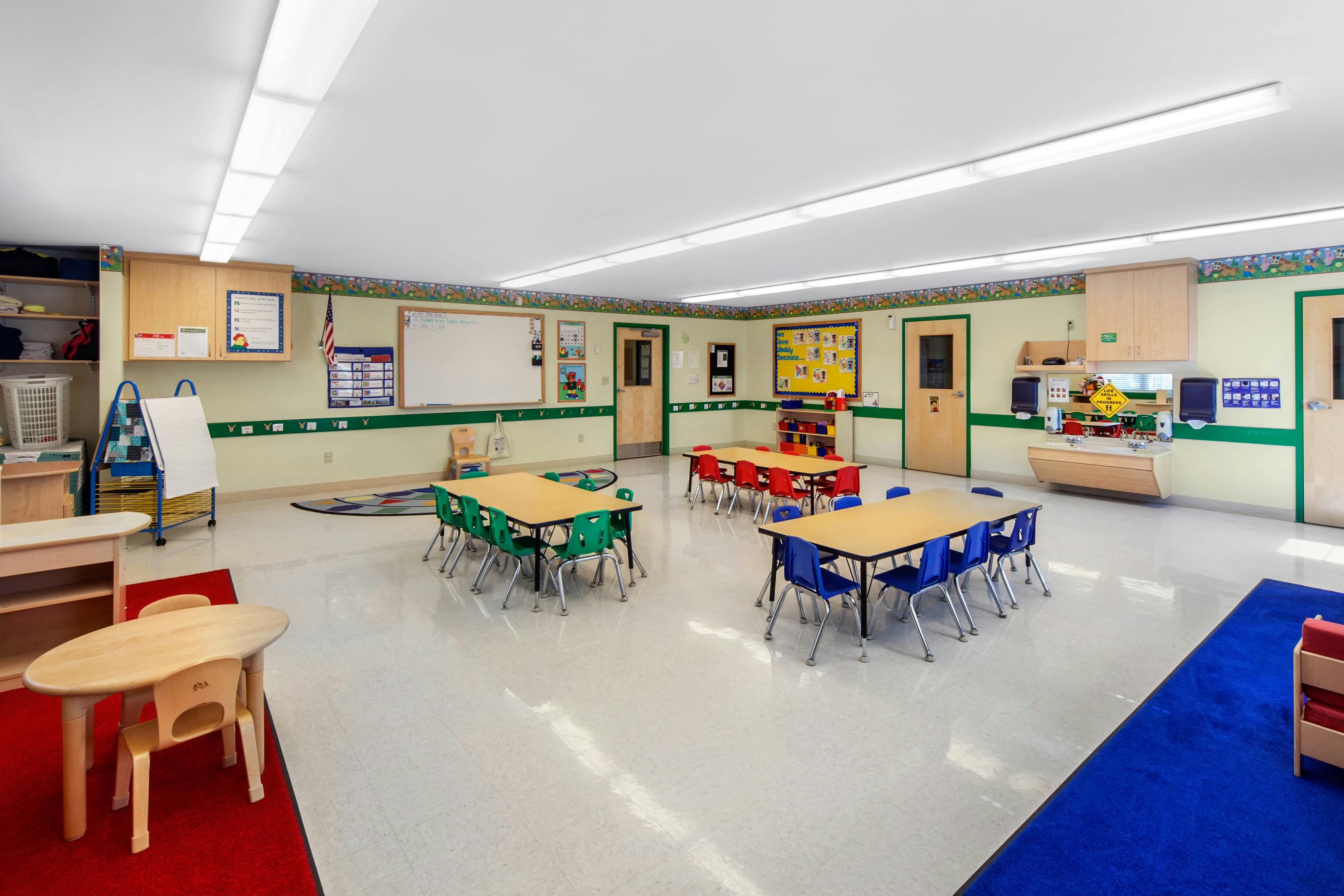Empty classroom with small tables and chairs, whiteboards, and a sink