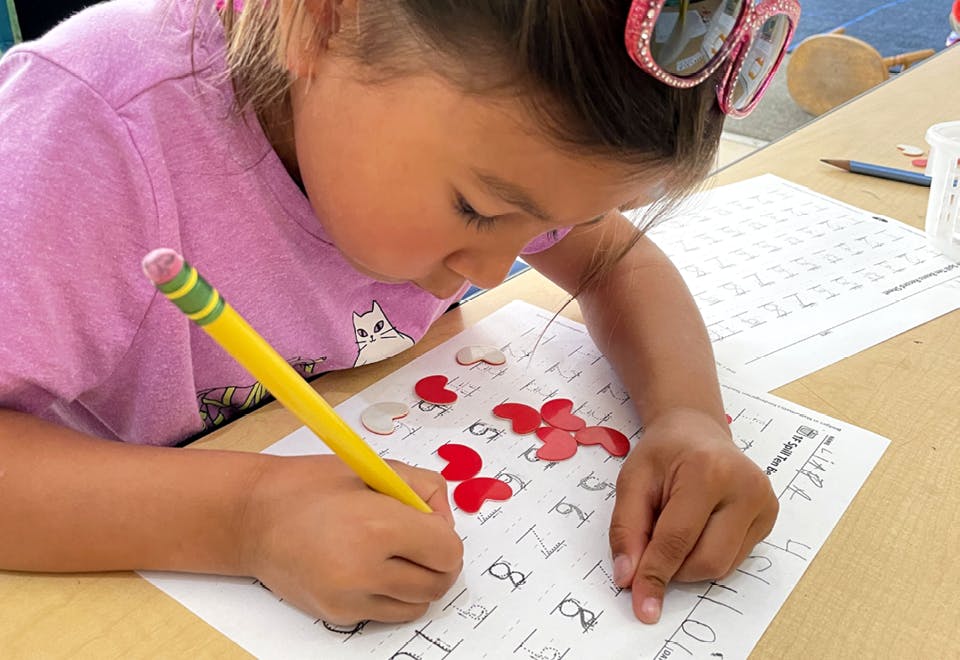 Child writing on paper with a pencil