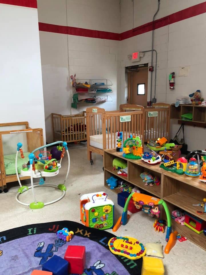 Nursery room with multiple cribs, a baby bouncer, and shelves of toys