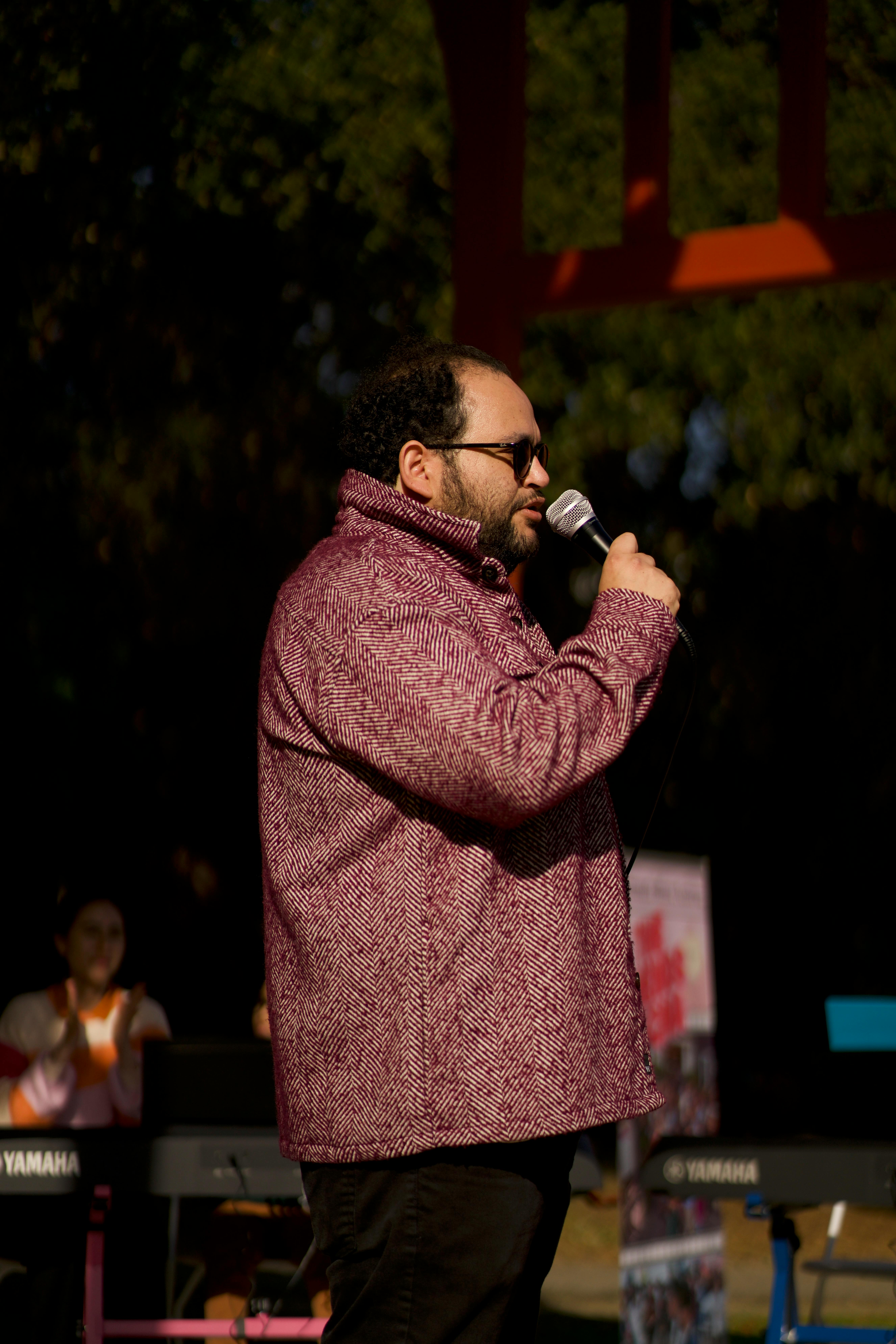 A person with a beard and sunglasses speaking into a microphone