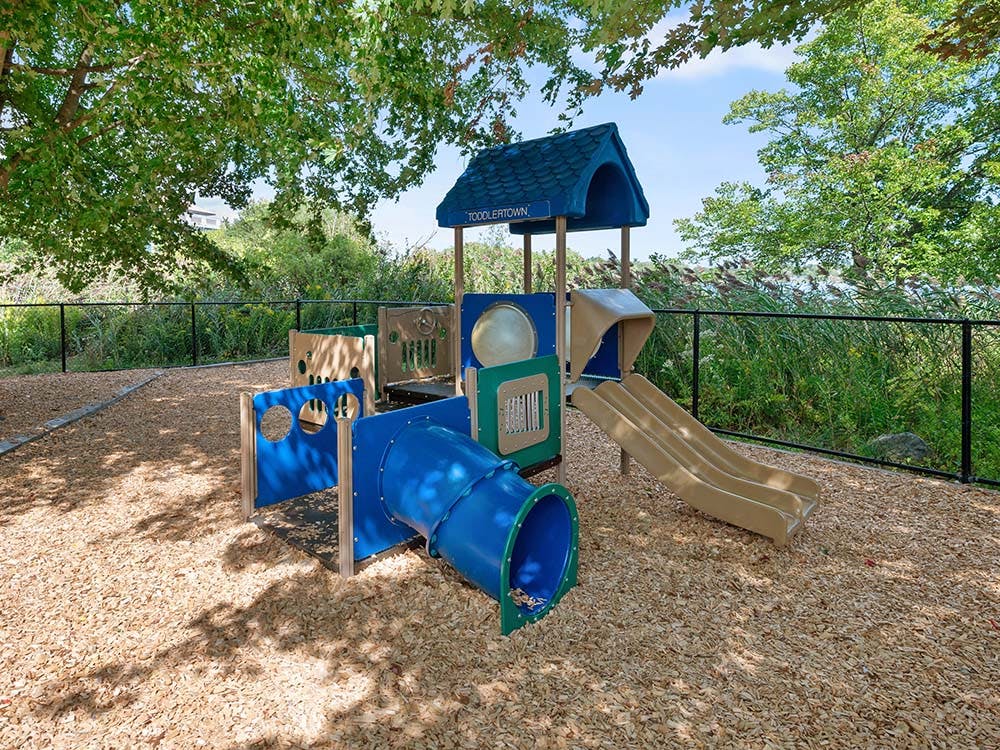 A colorful playground with slides and tunnels on wood chips under trees