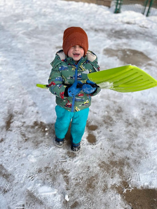 Child in winter clothing holding a bright green snow shovel