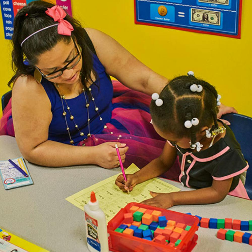 Adult and child writing at a table in a classroom