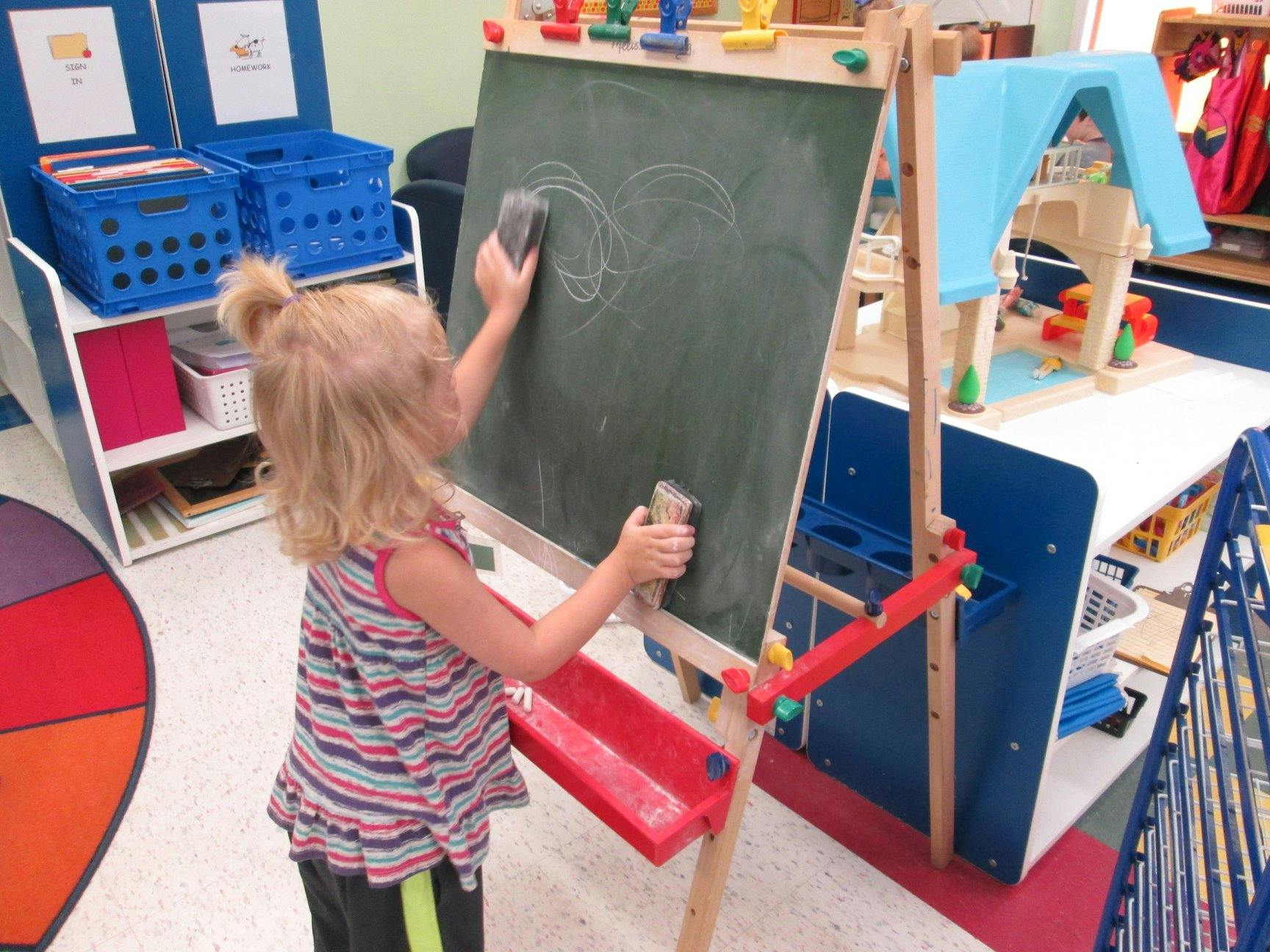 Child erasing a drawing on a chalkboard in a classroom