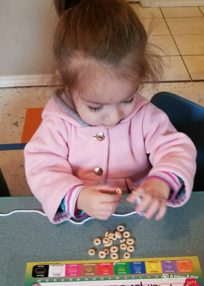 Child stringing cereal onto a piece of yarn