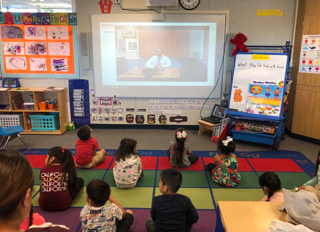 Children sitting on a rug watching a video projected on a screen in a classroom