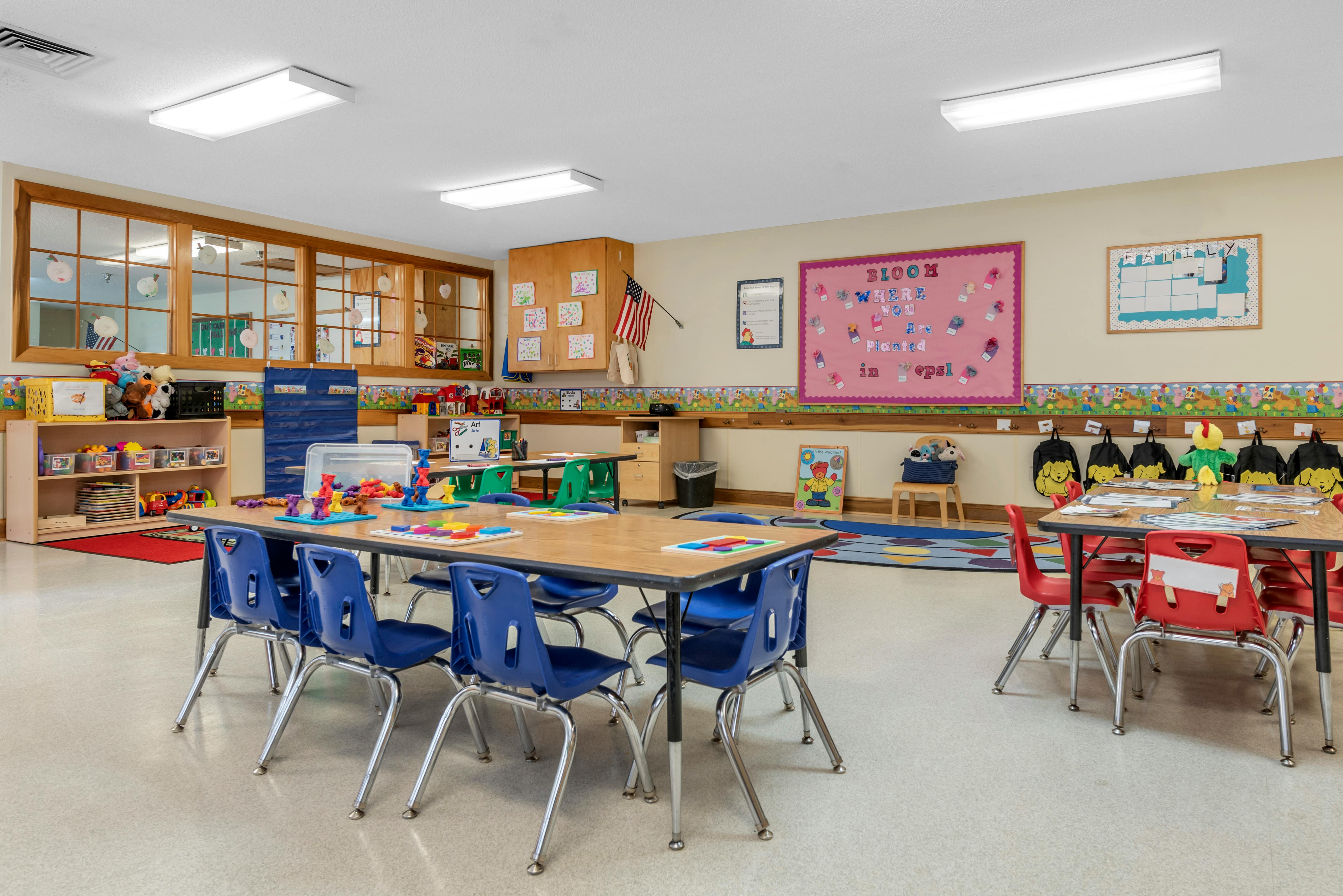 Classroom with child-sized tables and chairs, shelves with toys, and decorated walls