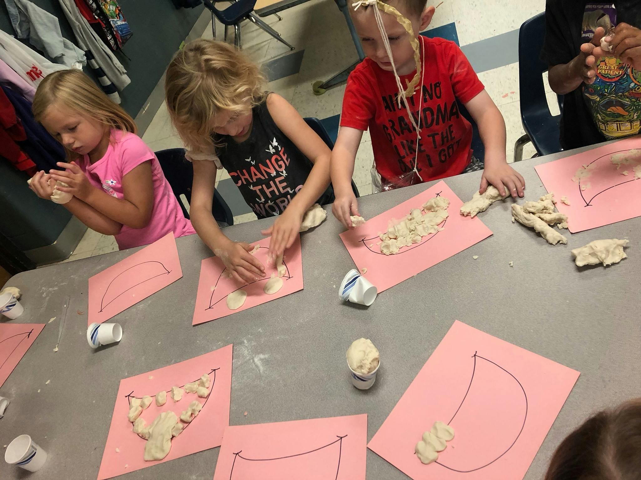 Children working with clay on pink paper in a classroom