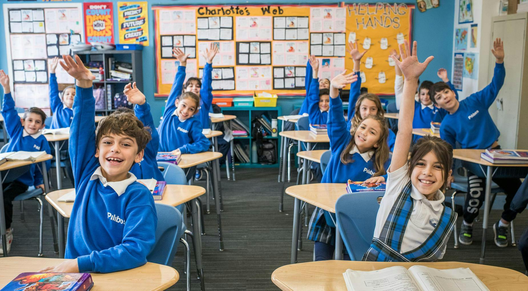 Children in blue shirts raising their hands in a classroom