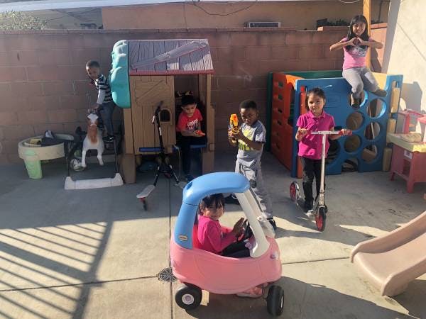 Children playing in a backyard with a toy car, scooter, and play structures