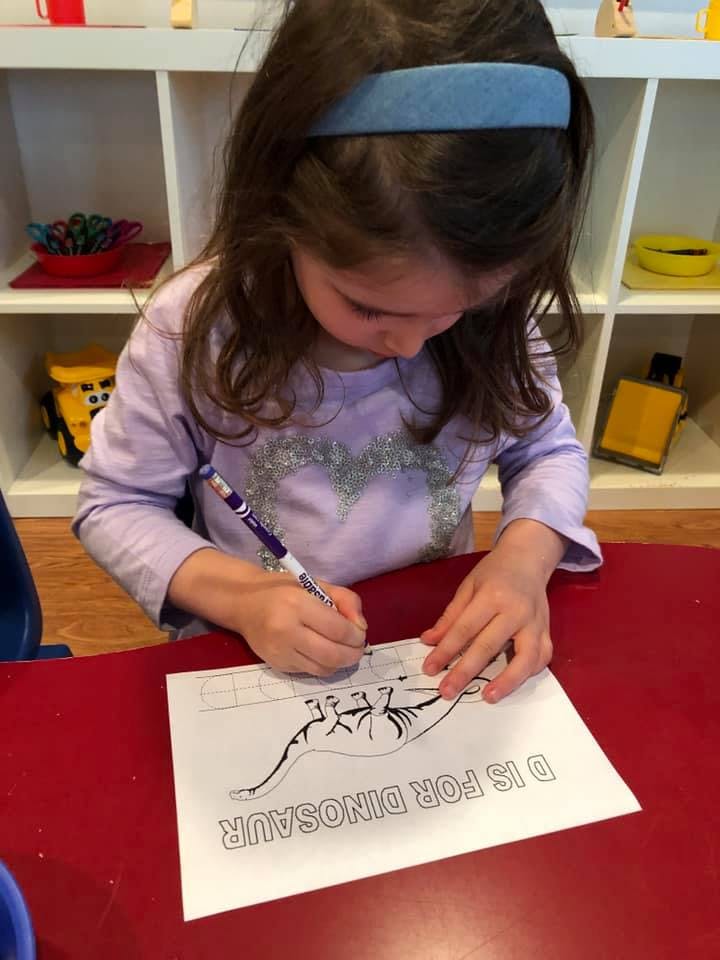 Child coloring a dinosaur picture with text "D IS FOR DINOSAUR"