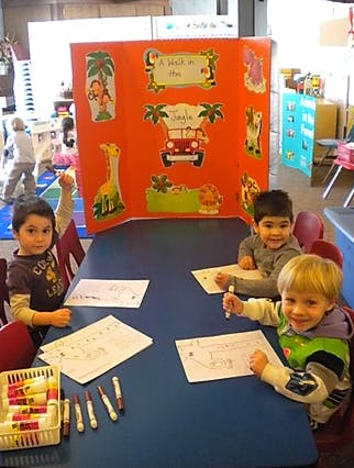 Three children drawing at a table in a classroom
