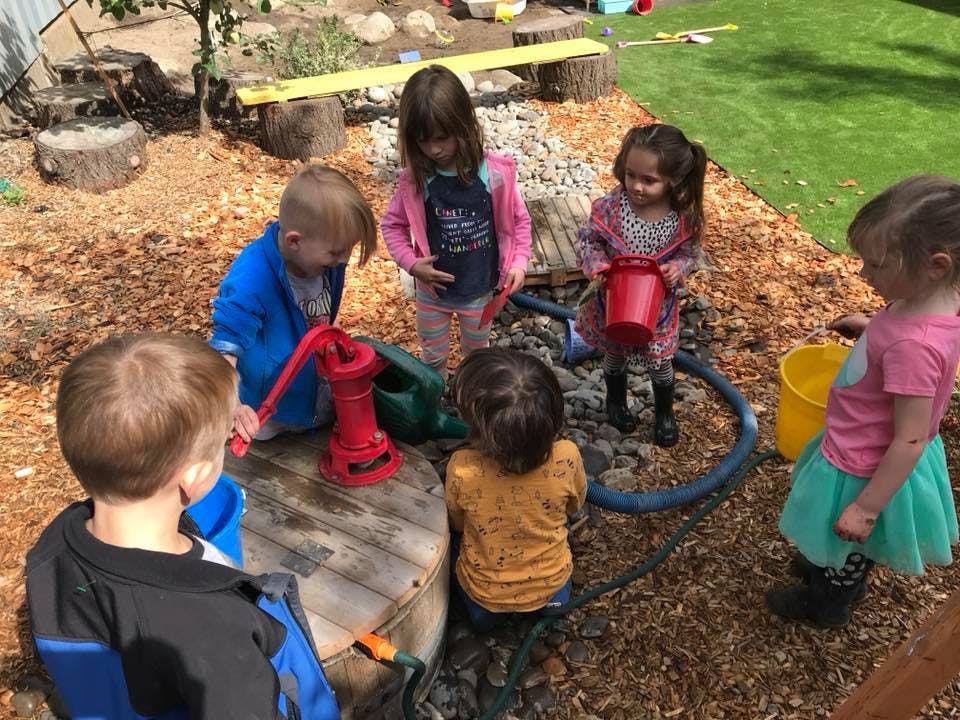 Children playing with a red water pump and buckets outdoors