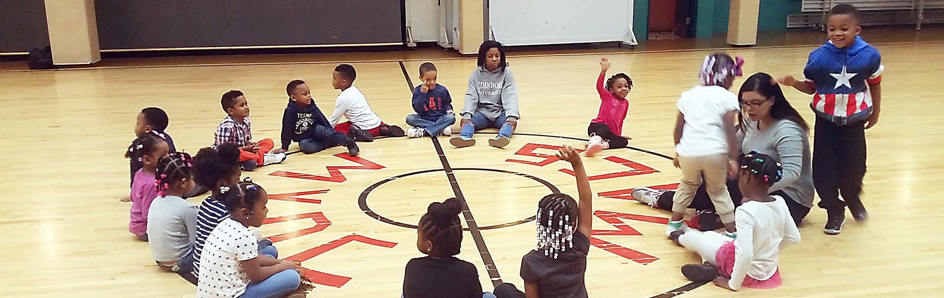 Children and adults sitting in a circle on a gym floor