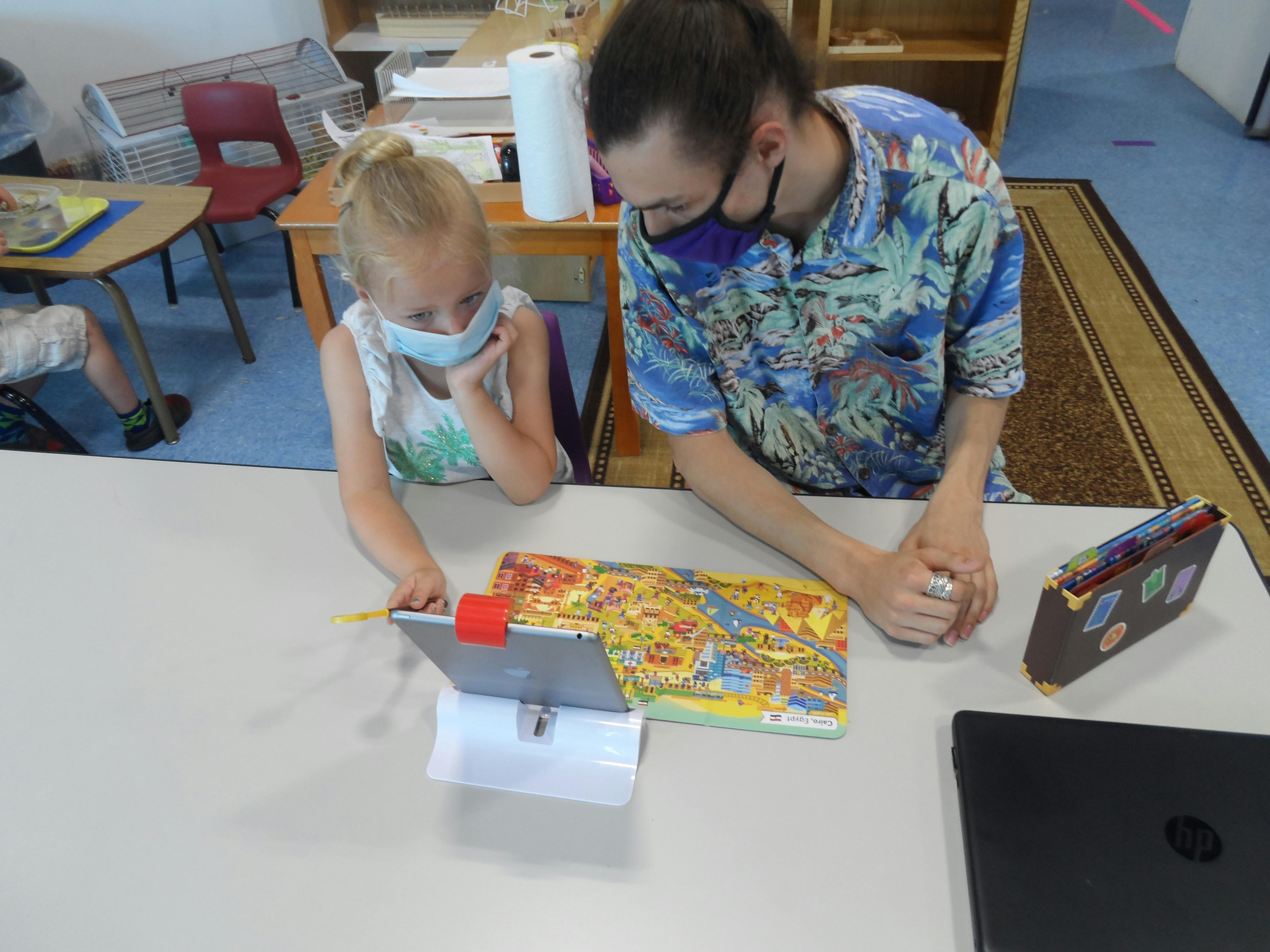 Person and child wearing masks looking at a tablet