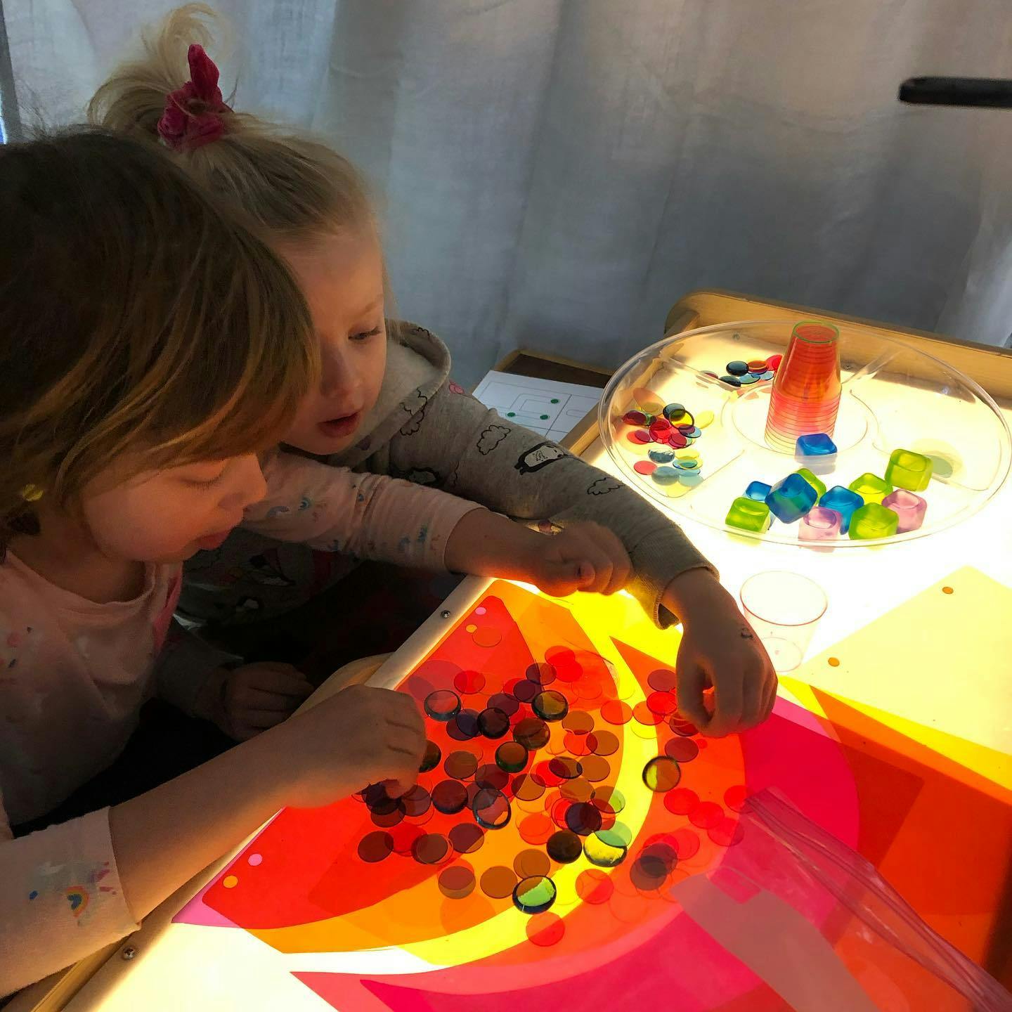 Two children playing with colorful translucent objects on a light table