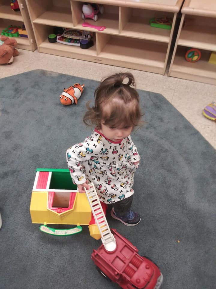 Child playing with a toy fire truck and ladder in a classroom