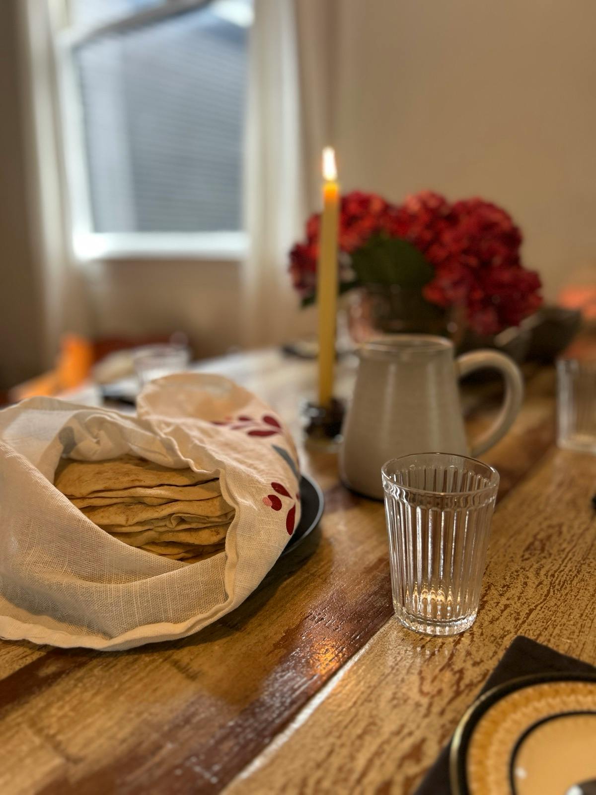 Tortillas wrapped in a cloth on a wooden table with a lit candle and flowers