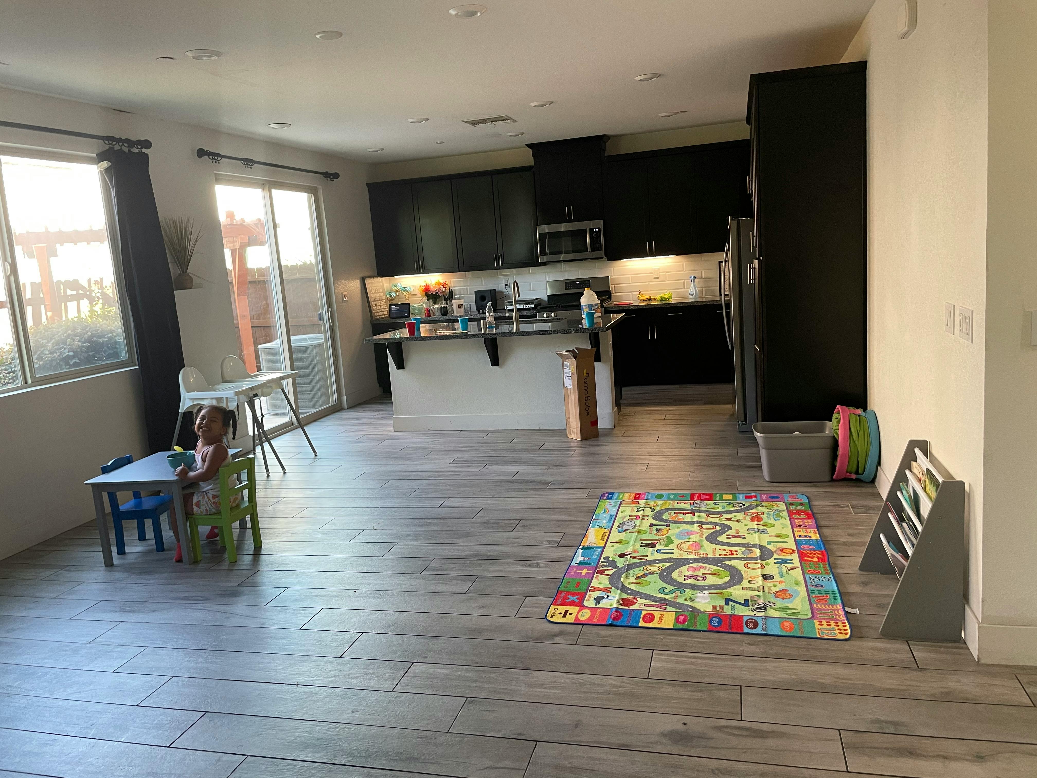 Child sitting at a small table in a room with a kitchen and playmat