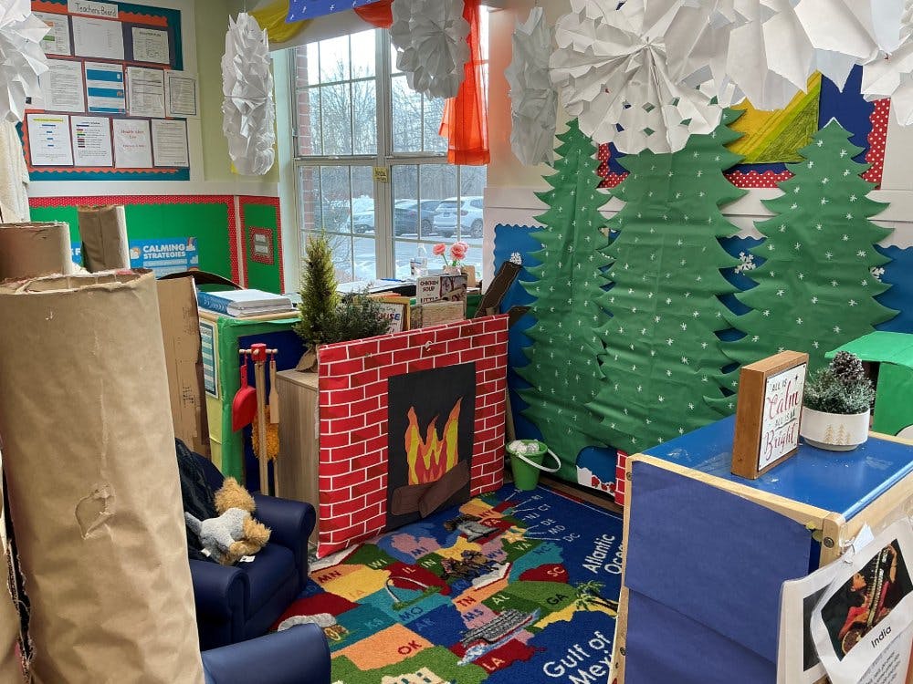 Classroom corner with map rug, a faux fireplace, and paper Christmas trees