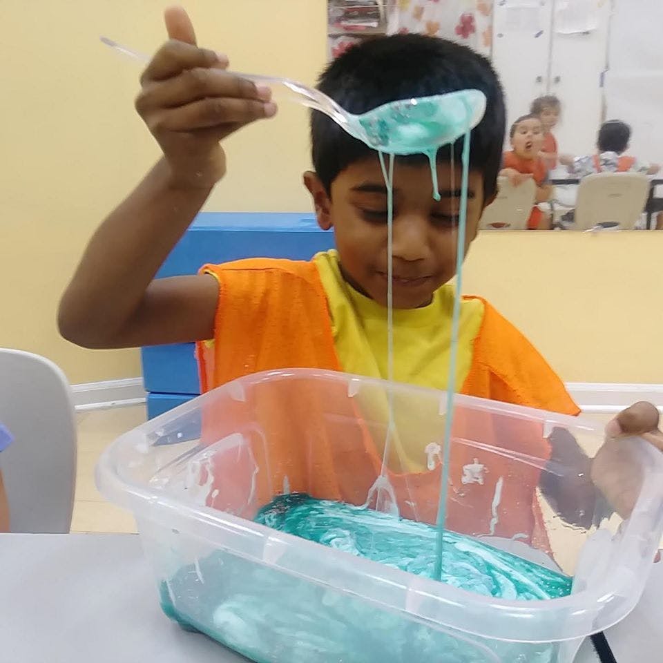 Child scooping blue slime from a container with a spoon