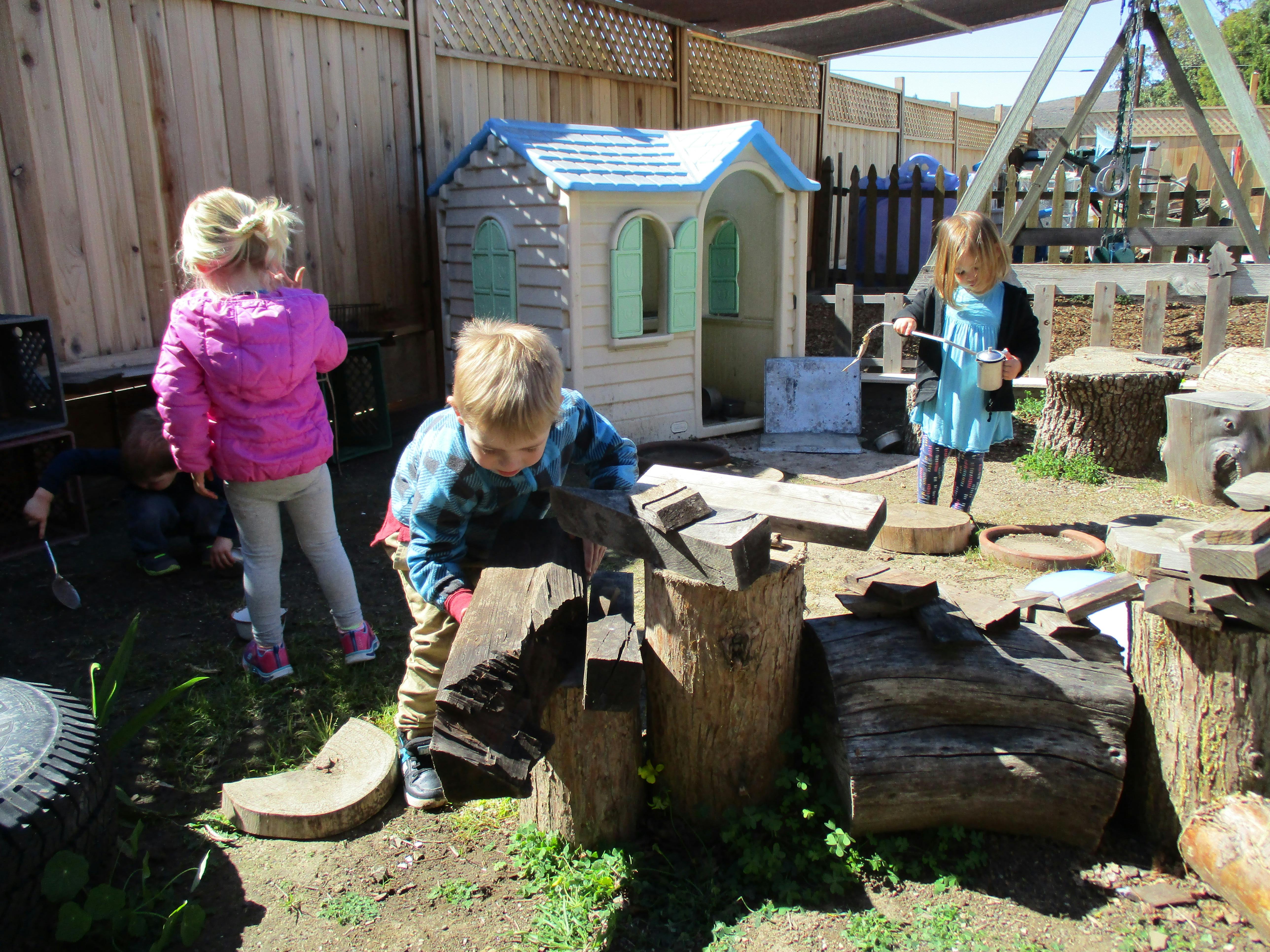 Child playing with wood blocks in a yard with other children