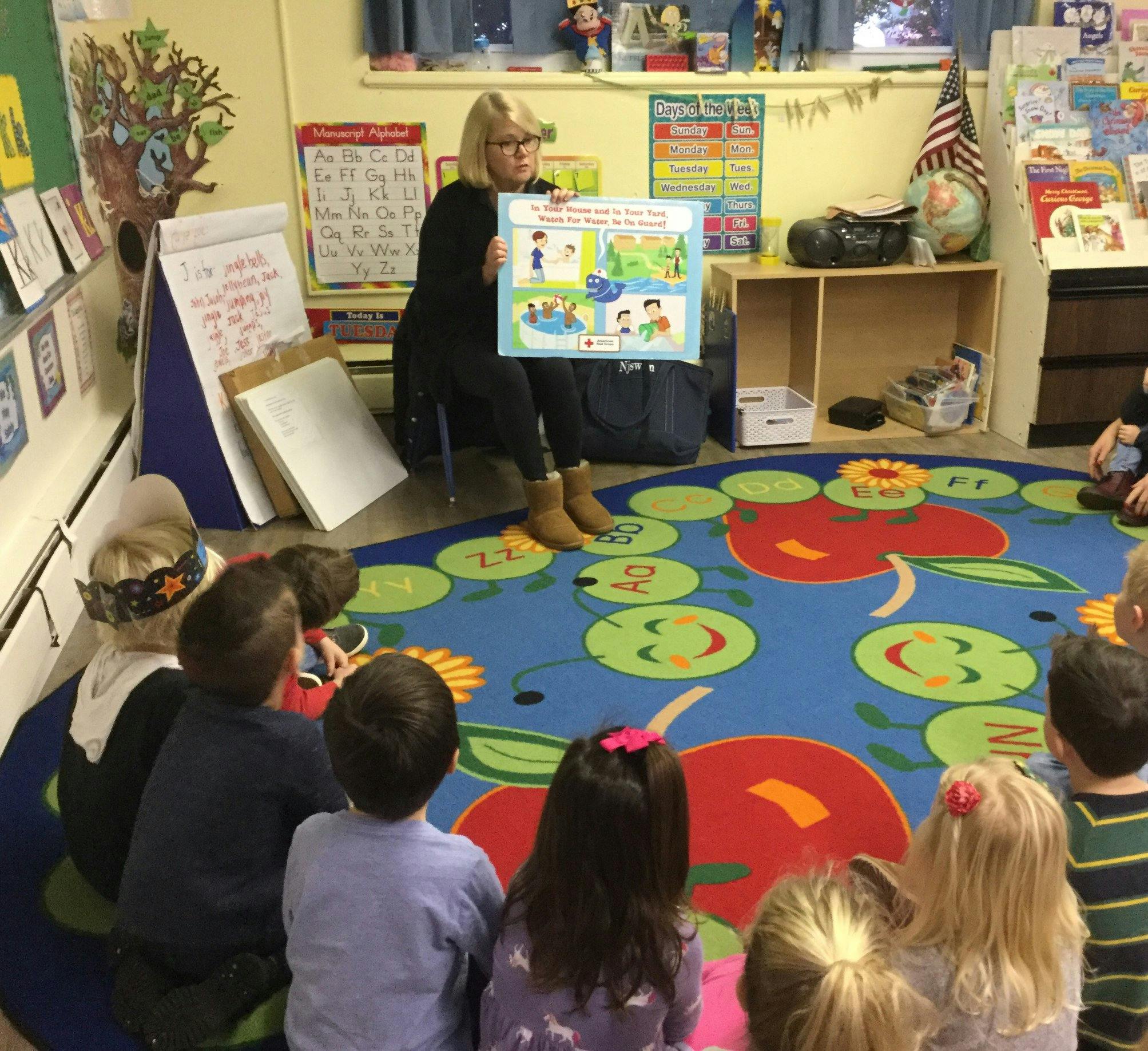 Person holding a poster for children sitting on a rug in a classroom