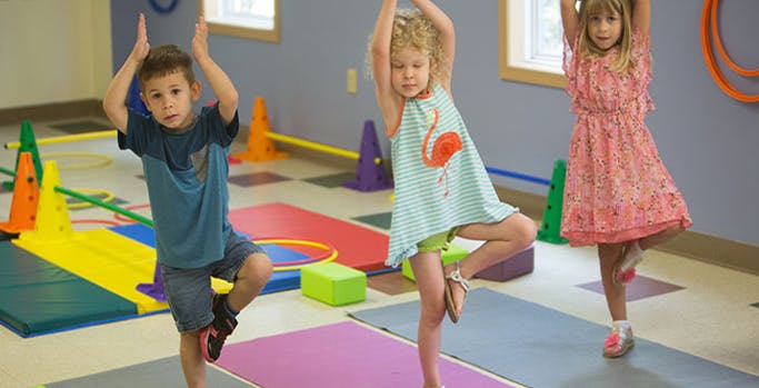 Three children doing a tree pose in a classroom