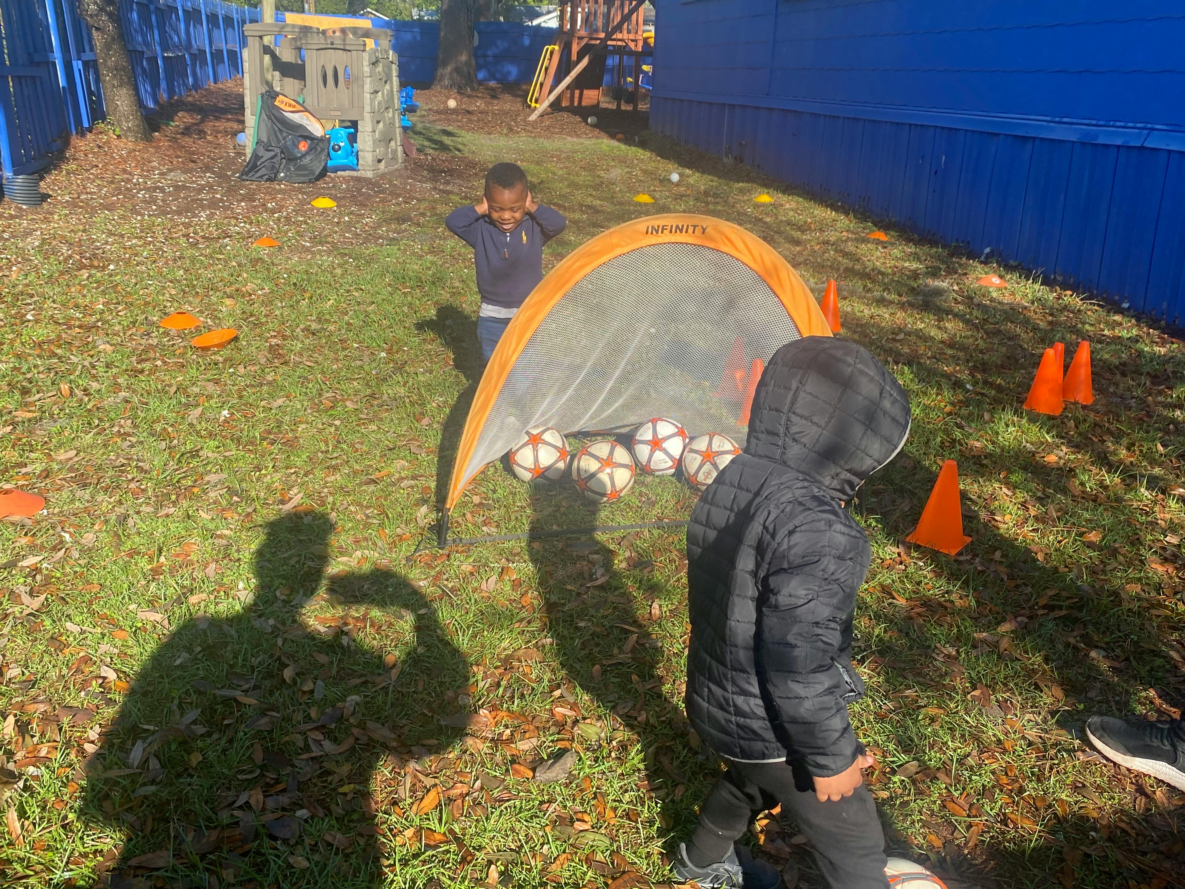 Children playing with soccer balls and a pop-up goal on a grassy playground
